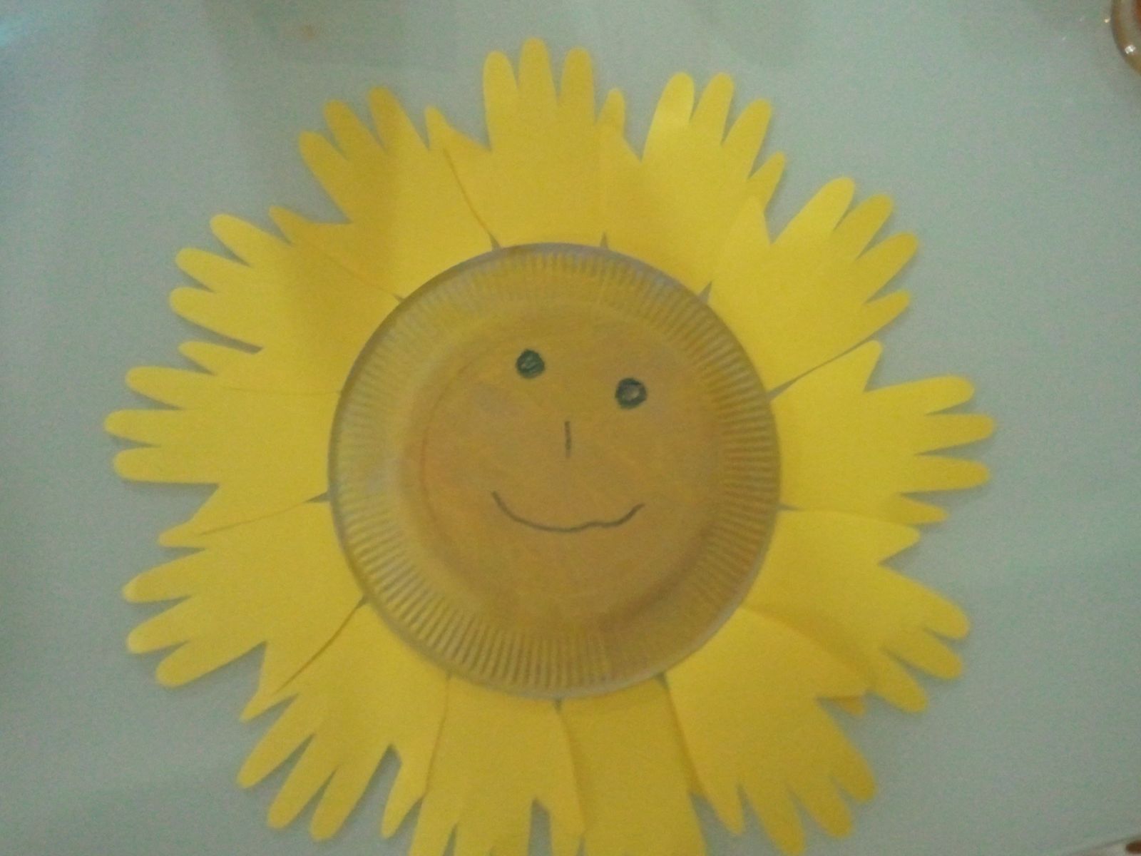 Des formes de main en papier jaune épais, un grand disque de carton peint en jaune (ou une assiette en carton)